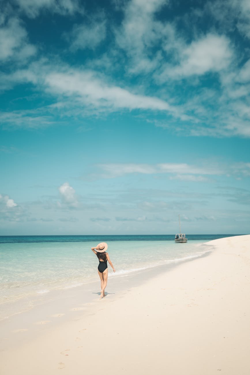 A serene moment capturing a woman strolling on a pristine beach in Zanzibar, Tanzania, under a bright blue sky.